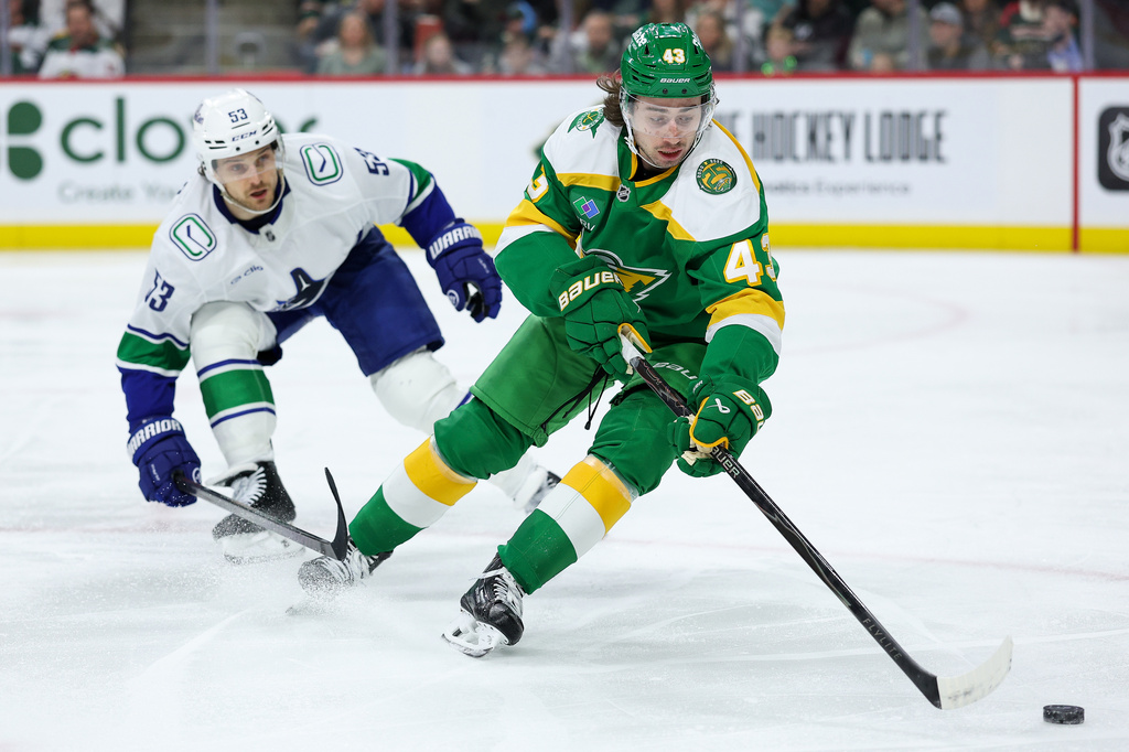 Minnesota Wild defenseman Quinn Hughes, right, skates with the puck as Vancouver Canucks center Teddy Blueger (53) defends during the second period of an NHL hockey game Thursday, April 2, 2026, in St. Paul, Minn. (AP Photo/Matt Krohn)