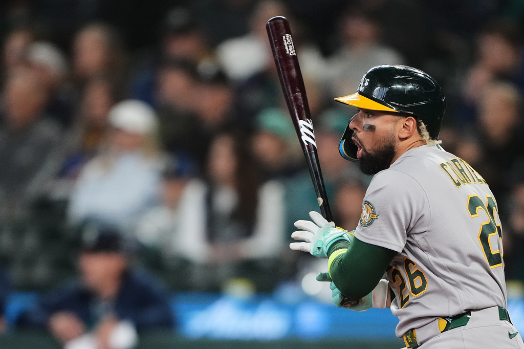 Athletics' Carlos Cortes reacts as he hits a line drive into the jersey of Seattle Mariners starting pitcher Logan Gilbert for a single during the first inning of a baseball game, Wednesday, April 22, 2026, in Seattle. (AP Photo/Lindsey Wasson)