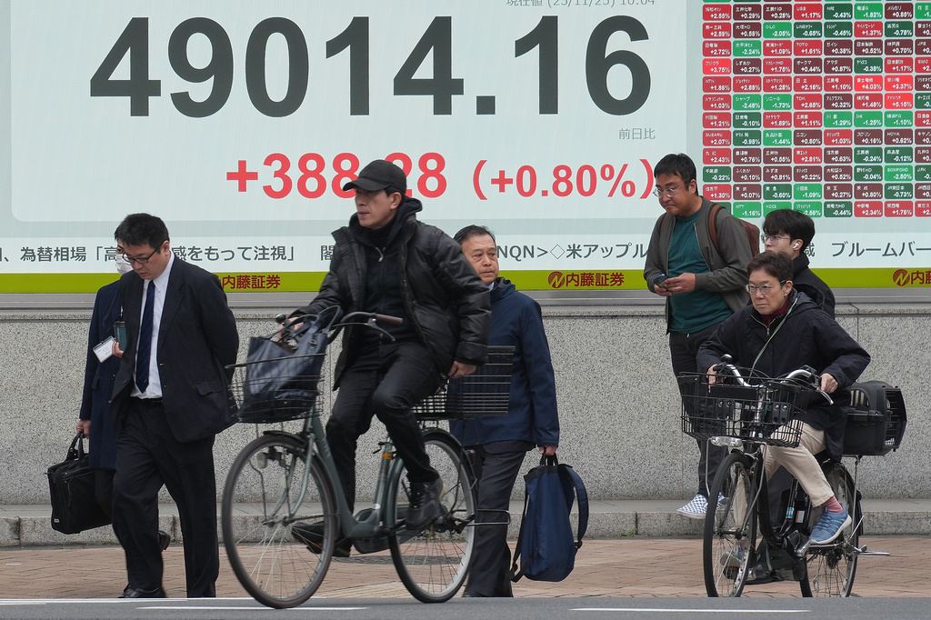 People cross a street near an electronic stock board showing Japan's Nikkei index at a securities firm Tuesday, Nov. 25, 2025, in Tokyo. (AP Photo/Eugene Hoshiko)
