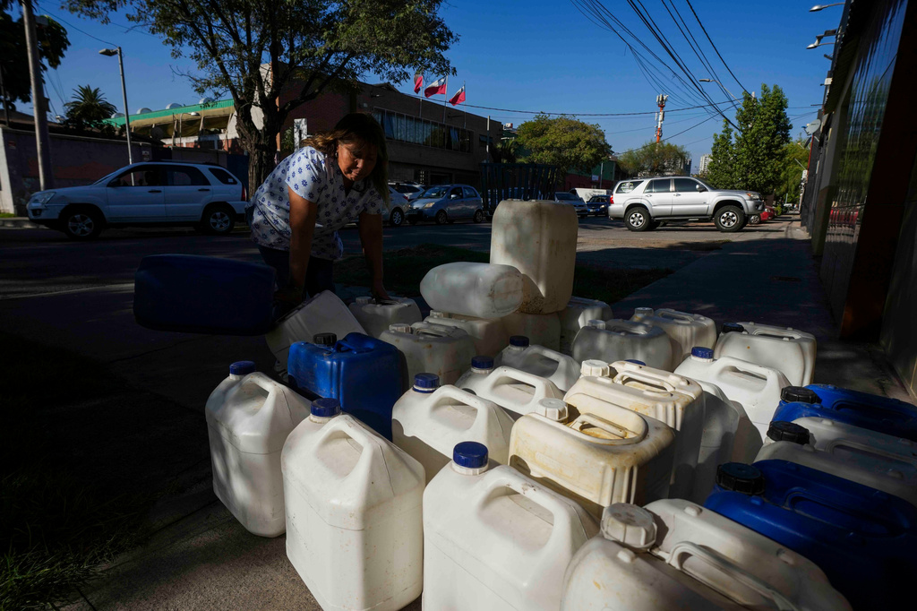 A woman sells portable gas tanks as drivers line up to fill their tanks in Santiago, Chile, Tuesday, March 24, 2026. (AP Photo/Esteban Felix)