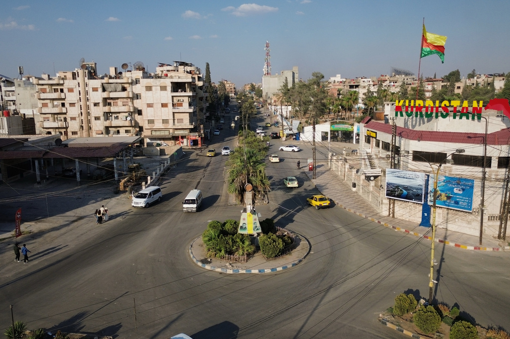 A flag bearing Kurdish colors flies above a building marked "Kurdistan" as traffic moves through an intersection in Qamishli, northeastern Syria, Wednesday, Aug. 26, 2026. (AP Photo/Baderkhan Ahmad)