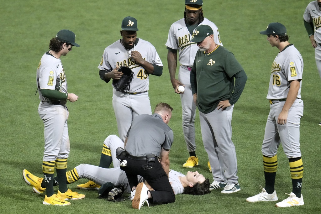 Athletics manager Mark Kotsay, second from right, watches as Zack Gelof, bottom, is tended to by a team trainer during the fifth inning of a baseball game against the Pittsburgh Pirates in Pittsburgh, Friday, Sept. 19, 2025. (AP Photo/Gene J. Puskar)