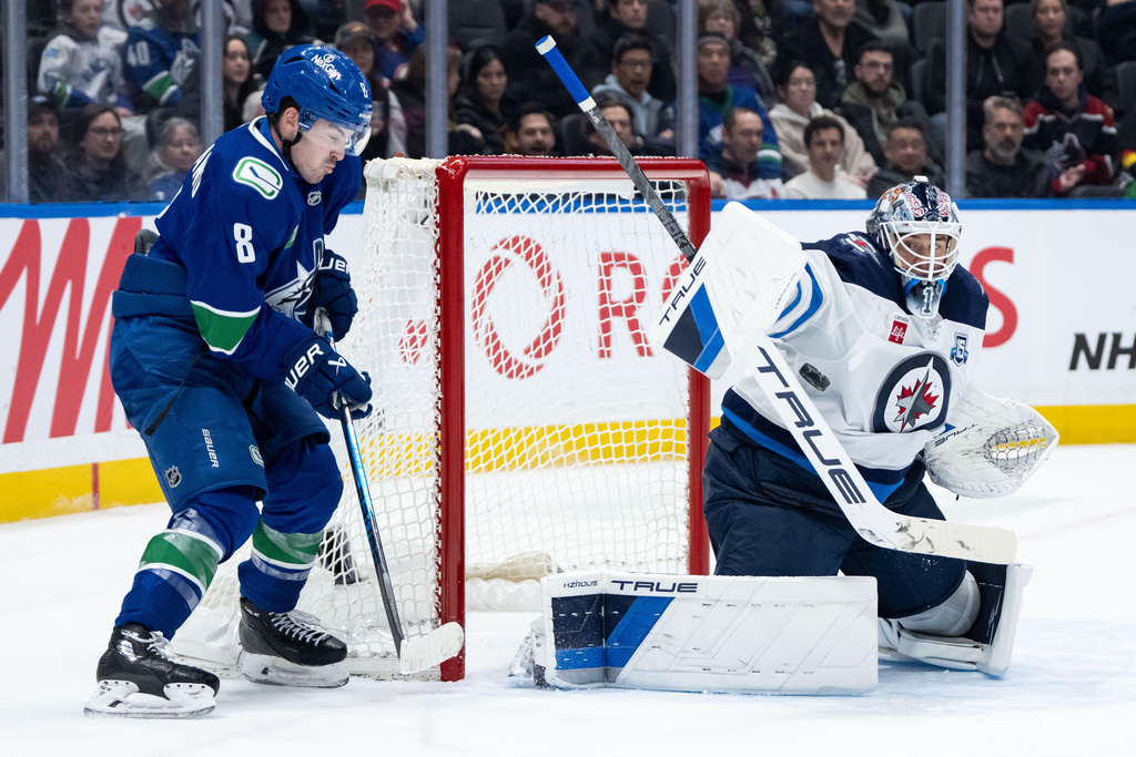Vancouver Canucks' Conor Garland (8) watches as Winnipeg Jets goaltender Eric Comrie (1) stops the puck during the third period of an NHL hockey game in Vancouver, B.C., on Wednesday, Feb. 25, 2026. (Ethan Cairns/The Canadian Press via AP)