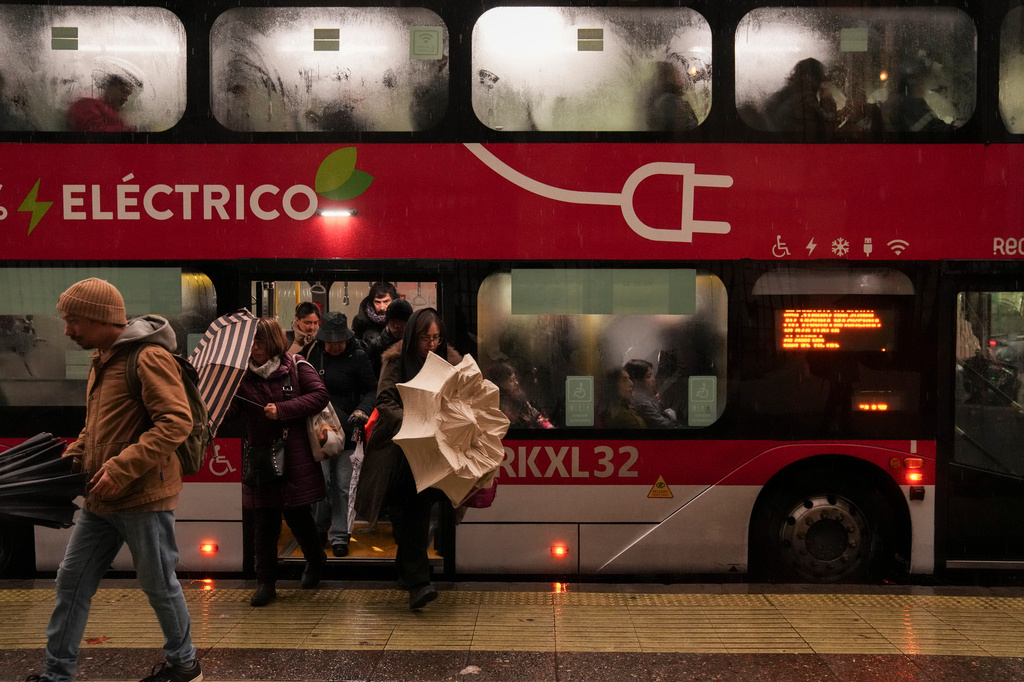 Commuters open their umbrellas as they leave the bus as it rains in Santiago, Chile, Monday, July 20, 2026. (AP Photo/Esteban Felix)