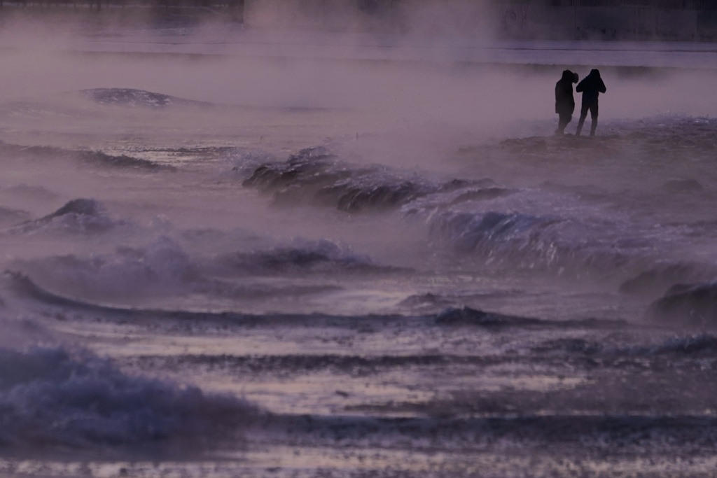 People walk on an ice covered beach along the shore of Lake Michigan, Friday, Jan. 23, 2026, in Chicago. (AP Photo/Kiichiro Sato)