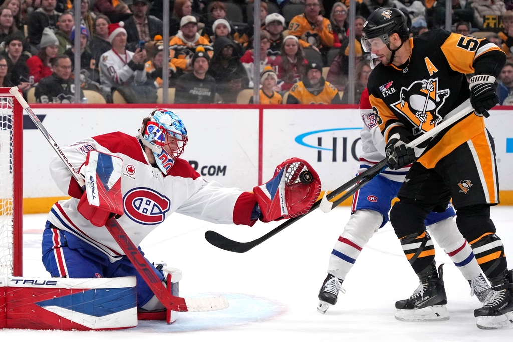 Montréal Canadiens goaltender Jakub Dobes, left, gloves a shot with Pittsburgh Penguins' Kris Letang, right, looking for a rebound and Cole Caufield, rear right, defending during the second period of an NHL hockey game in Pittsburgh, Sunday, Dec. 21, 2025. (AP Photo/Gene J. Puskar)