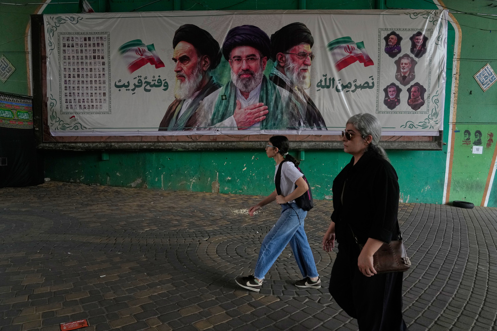 Women walk past a banner showing portraits of the late Iranian revolutionary founder Ayatollah Khomeini, left, Supreme Leader Ayatollah Mojtaba Khamenei, center, and the late Supreme Leader Ayatollah Ali Khamenei, who was killed in the U.S. and Israel strike on Feb. 28, under a bridge in northern Tehran, Iran, Sunday, Aug. 2, 2026. (AP Photo/Vahid Salemi)