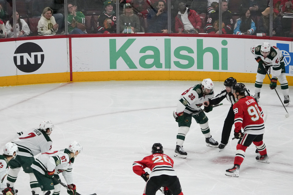 A face-off during the third period of an NHL hockey game between the Chicago Blackhawks and the Minnesota Wild with the Kalshi sign in the background Tuesday, March, 17, 2026, in Chicago. (AP Photo/David Banks)
