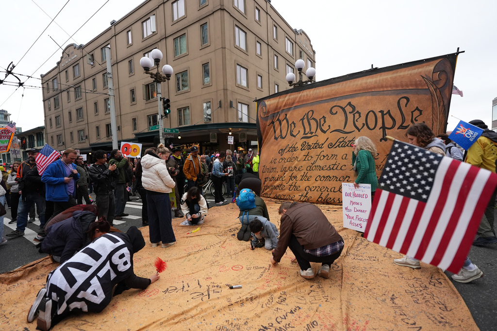 People are signing a giant Constitution as they take part in a "No Kings" protest Saturday, Oct. 18, 2025, in Seattle. (AP Photo/Lindsey Wasson)