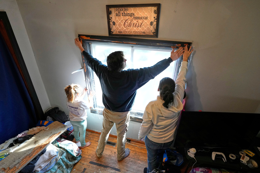 Gerard Berry, along with his wife, Stephanie, and daughter, Brooklynn, cover a bedroom window with plastic, Friday, Nov. 7, 2025, in Baileyville, Maine. (AP Photo/Robert F. Bukaty)