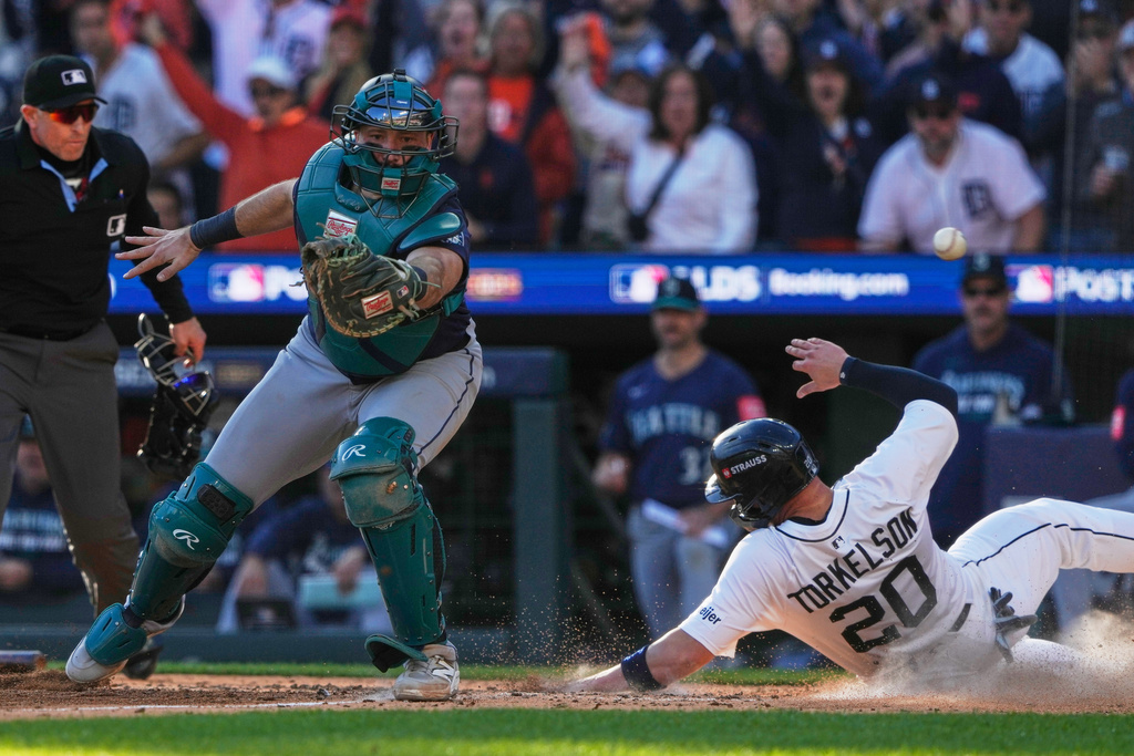 Detroit Tigers' Spencer Torkelson (20) scores past Seattle Mariners catcher Cal Raleigh during the sixth inning in Game 4 of baseball's American League Division Series Wednesday, Oct. 8, 2025, in Detroit. (AP Photo/Ryan Sun)