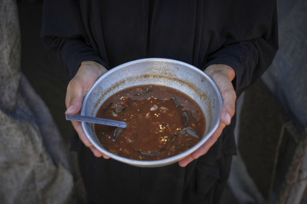 Palestinian woman Sally Muzhed, 38, displaced from Deir al-Balah, poses for a picture holding a plate with eggplant, her only food for the day, amid severe food shortages in the Gaza Strip, in Deir al-Balah, Monday, Aug. 4, 2025. (AP Photo/Abdel Kareem Hana)