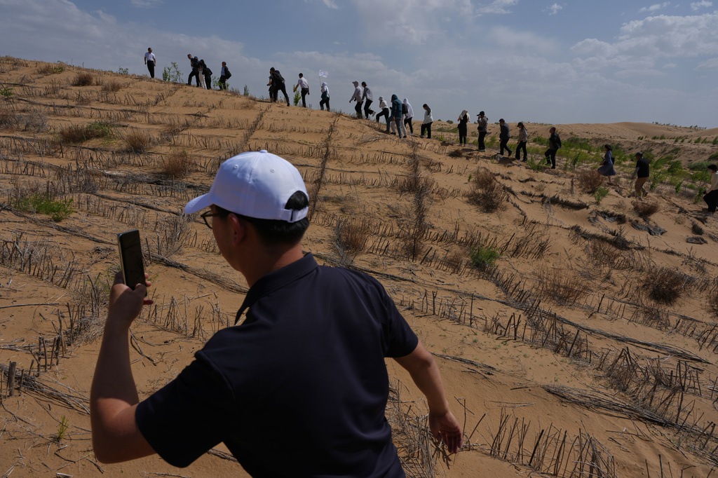 Visitors walk past a grass checkerboard on a sand dune that is part of desertification control efforts at the Engebei Ecological Area near Ordos in northern China's Inner Mongolia province on Friday, June 12, 2026. (AP Photo/Ng Han Guan)