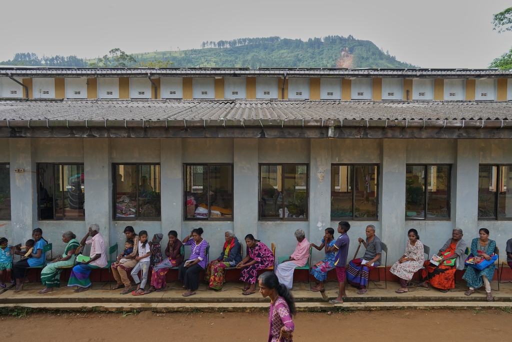 Displaced tea plantation workers and their families queue for aid at a safety center after Cyclone Ditwah led to floods and landslides at Craighead Estate in Nawalapitiya, Sri Lanka, Friday, Dec. 12, 2025. (AP Photo/Eranga Jayawardena)