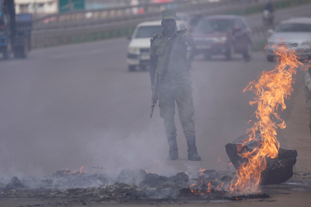 A Ugandan police officer makes a gesture behind a burning fire amid protests following the announcement of the preliminary results in Kampala, Uganda, Friday, Jan. 16, 2026. (AP Photo/Brian Inganga)