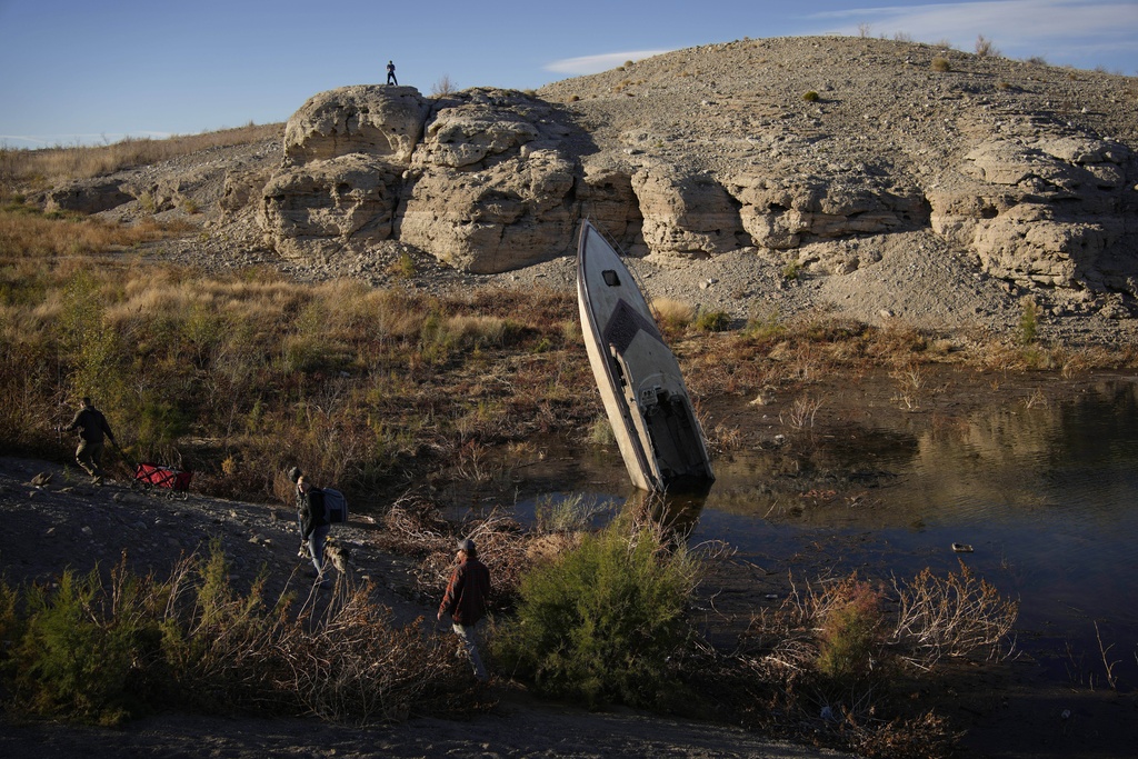FILE - People walk by a formerly sunken boat standing upright along the shoreline of Lake Mead at the Lake Mead National Recreation Area, Jan. 27, 2023, near Boulder City, Nev. (AP Photo/John Locher, File)