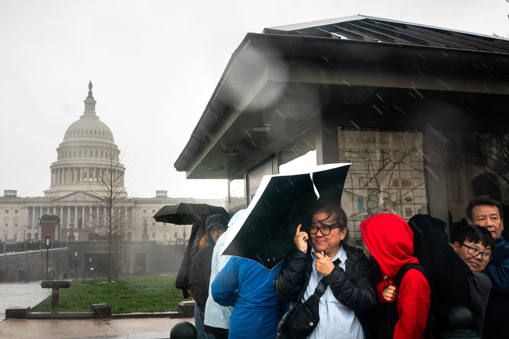 Visitors take cover during heavy rain near the U.S. Capitol on Capitol Hill in Washington, Monday, March. 16, 2026. (AP Photo/Nathan Howard)