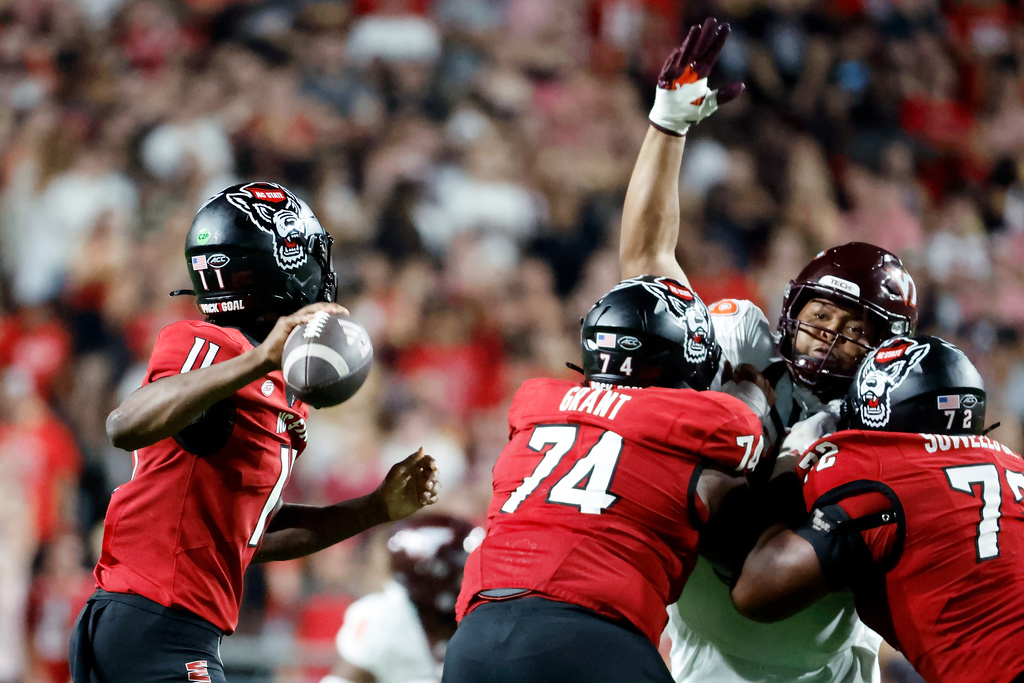 North Carolina State quarterback CJ Bailey (11) tries to throw the ball over Virginia Tech defensive lineman Emmett Laws (99) being guarded by North Carolina State offensive lineman Jalen Grant (74) and Spike Sowells, right, during the first half of an NCAA college football game in Raleigh, N.C., Saturday, Sept. 27, 2025. (AP Photo/Karl DeBlaker)