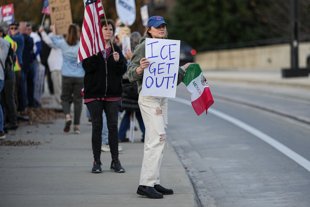 Protesters hold signs amid the arrival of federal law enforcement, Tuesday, Nov. 18, 2025, in Charlotte, N.C. (AP Photo/Matt Kelley)