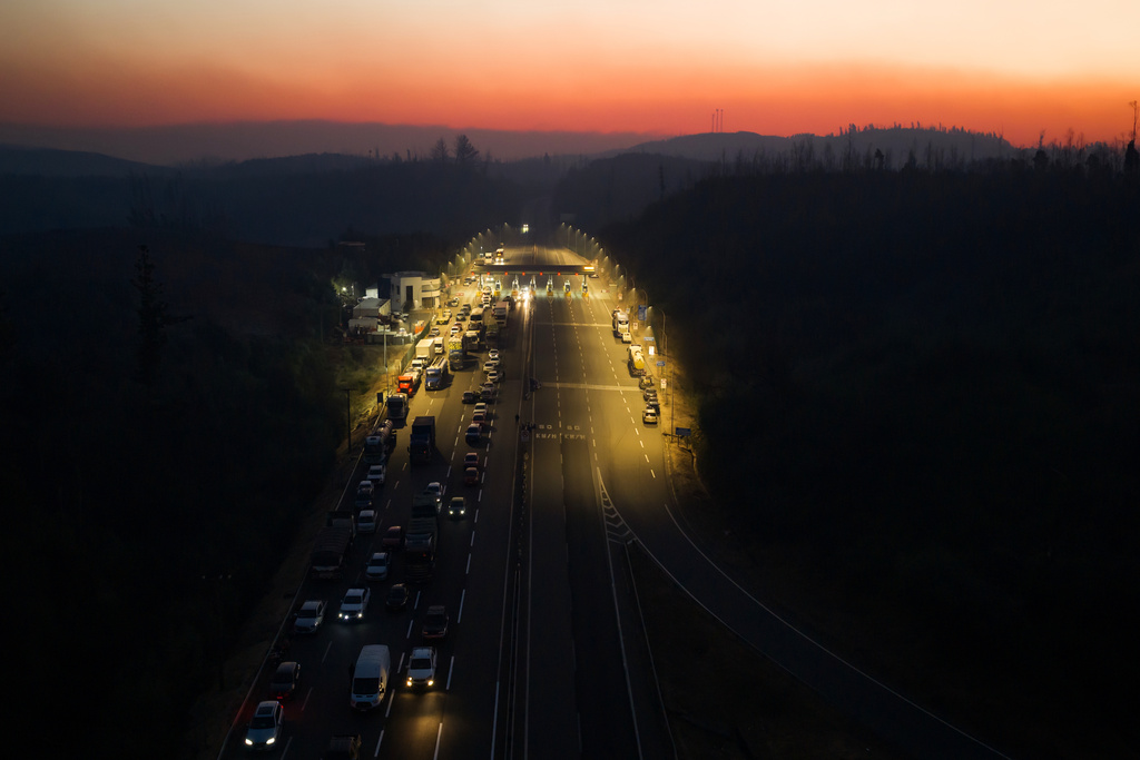 Vehicles stop at a toll plaza at sunrise as wildfires burn near Lirquen, Chile, Sunday, Jan. 18, 2026. (AP Photo/Javier Torres)