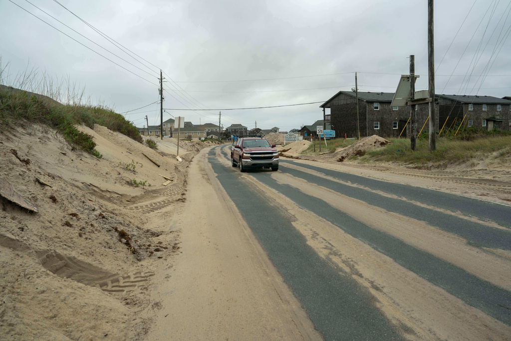 A car drives over sand on Highway 12 after a storm, Monday, Oct. 13, 2025, in Buxton, N.C. (AP Photo/Allison Joyce)