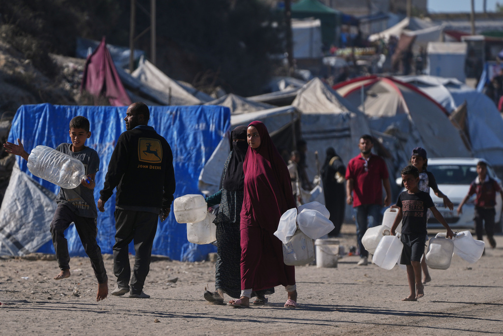 Palestinians carry plastic bottles to collect water in an area of a makeshift tent camp for displaced people along the shore of Nuseirat, in the central Gaza Strip, Wednesday, Oct. 8, 2025. (AP Photo/Abdel Kareem Hana)