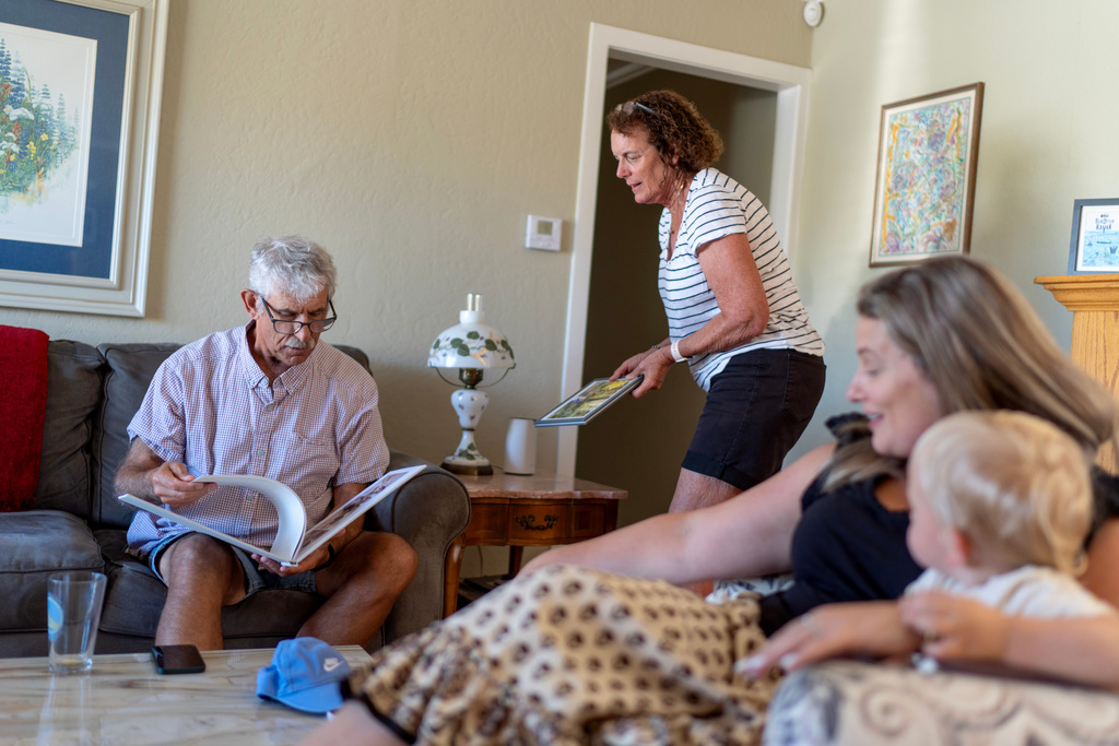 Christy Morrill, 72, left, who lost decades of memories to autoimmune encephalitis, looks over family photo albums with, from left, his wife Karen, daughter Caitlin and grandson Colter, at his home, Tuesday, Aug. 19, 2025, in San Carlos, Calif. (AP Photo/David Goldman)