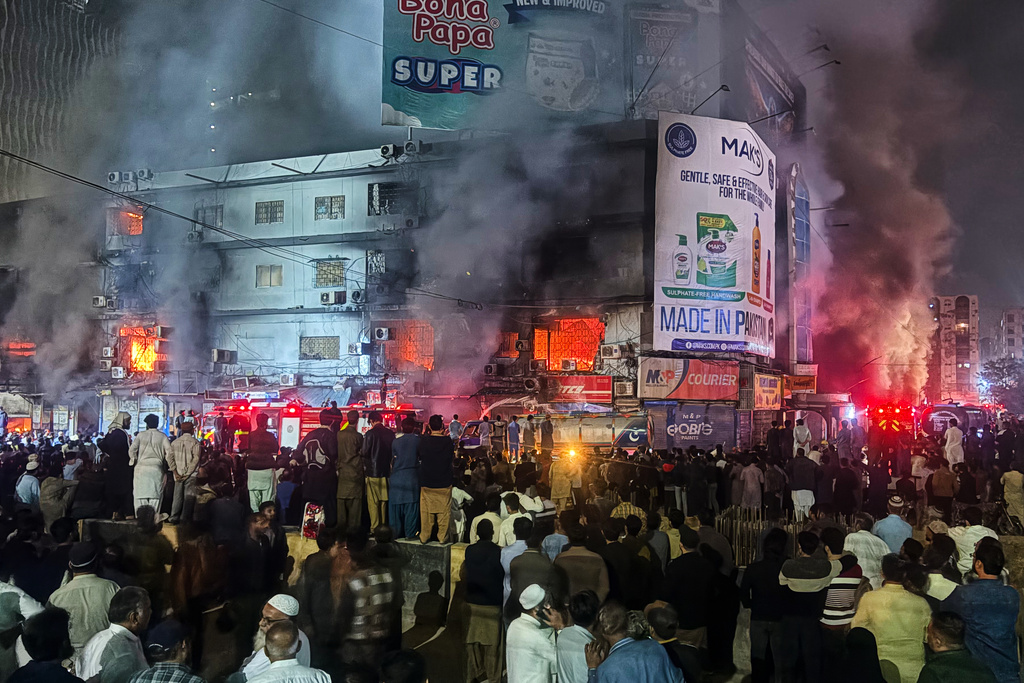 People gather as firefighters try to control a massive fire that broke out in a multi-story shopping mall, in Karachi, Pakistan, Sunday, Jan. 18, 2026. (AP Photo/Mohammad Farooq)