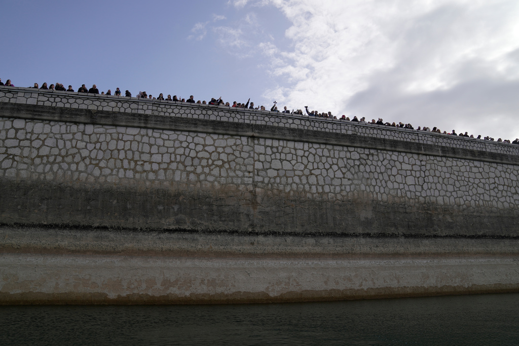 People attend the Epiphany ceremony as a Greek Orthodox priest, center, holding a cross blesses the waters at Lake Marathon, near Athens, on Tuesday, Jan. 6, 2026, where receding water levels reflect successive years of low rainfall across Greece. (AP Photo/Thanassis Stavrakis)