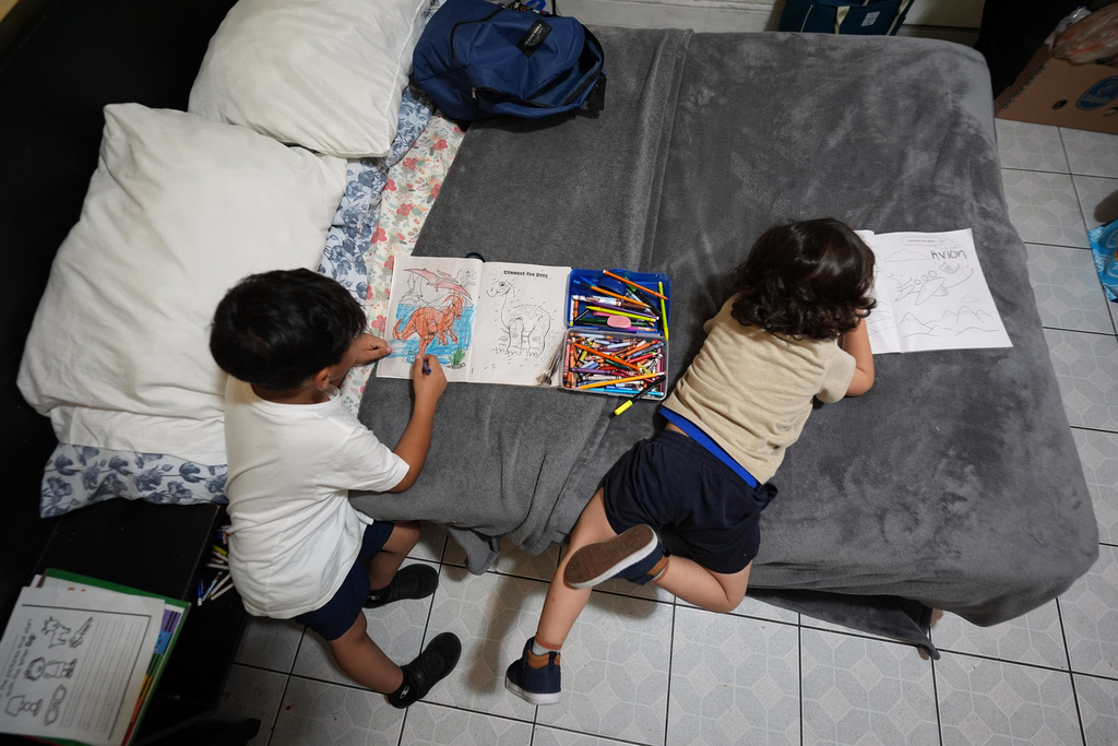Jakelin Pasedo's sons, ages 5 and 3, color on the bed inside the Miami-area motel room where the trio live, all of whom have refugee status, Wednesday, Oct. 22, 2025, after their father requested to be sent back to Venezuela after months in immigration detention. (AP Photo/Rebecca Blackwell)