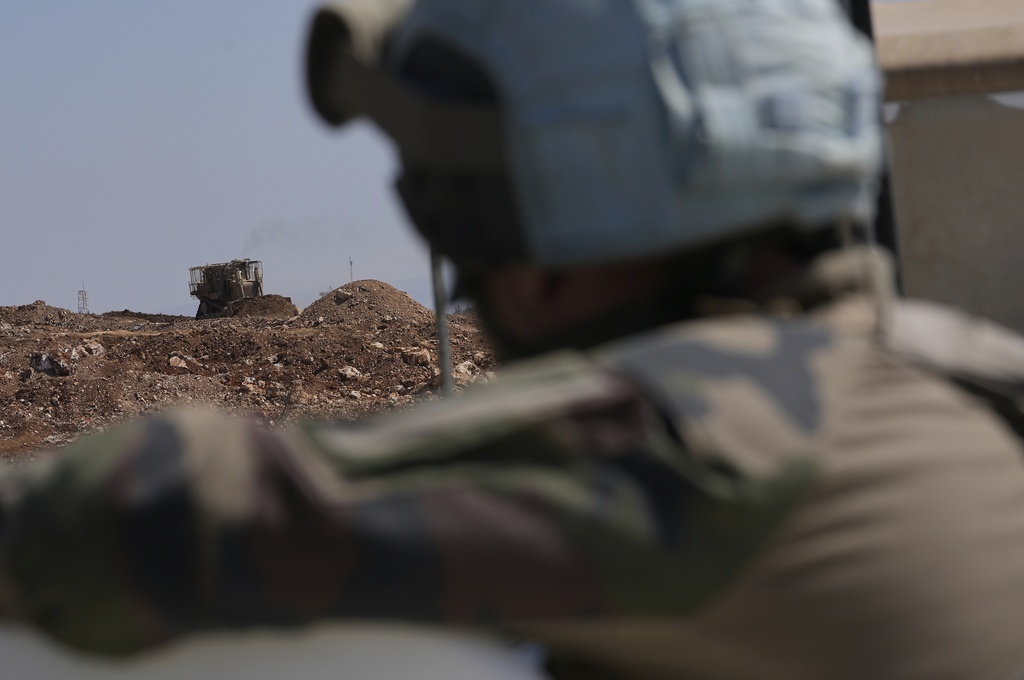 A French U.N. peacekeeper, foreground, watches an Israeli bulldozer building a sand barrier at one of five new Israeli army positions along the road between Houla and Kfar Kila, southern Lebanon, Wednesday, Aug. 20, 2025, following airstrikes and a ground offensive that destroyed nearby villages. (AP Photo/Hussein Malla)