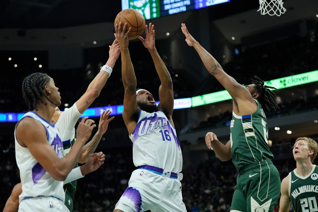 Utah Jazz's Elijah Harkless (16) looks to shoot between Milwaukee Bucks' Cam Thomas, second from right, and Ryan Rollins, back left, during the first half of an NBA basketball game Saturday, March 7, 2026, in Milwaukee. (AP Photo/Aaron Gash)