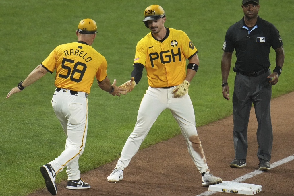 Pittsburgh Pirates' Bryan Reynolds, center, celebrates with third base coach Mike Rabelo (58) as Reynolds stands on third base after driving in two runs with a triple off Cincinnati Reds pitcher Tony Santillan during the eighth inning of a baseball game in Pittsburgh, Friday, Aug. 8, 2025. (AP Photo/Gene J. Puskar)