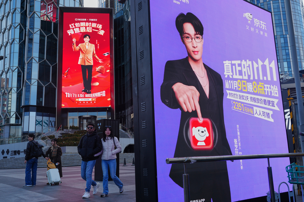 People walk by advertisement billboards promoting Chinese e-commerce platform JD.com, right, and Tmall, left, on their Singles' Day sale at a popular shopping district in Beijing on Nov. 10, 2025. (AP Photo/Andy Wong)