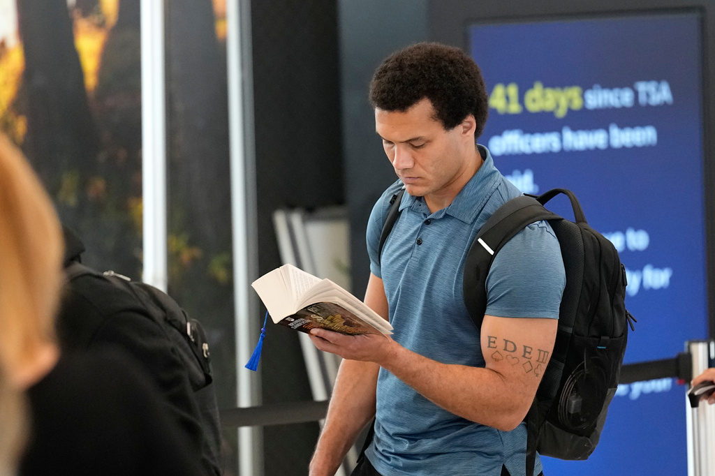 A traveler reads a book while waiting in long security checkpoint lines at George Bush Intercontinental Airport Friday, March 27, 2026, in Houston. (AP Photo/David J. Phillip)