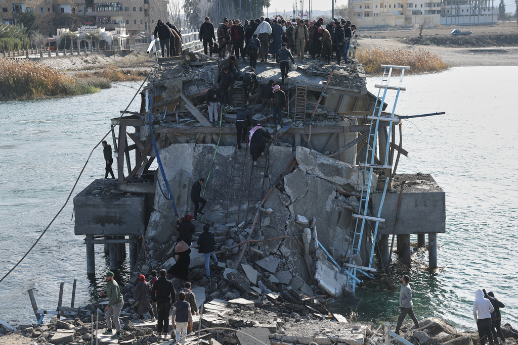 People climb over the damaged Al-Rashid Bridge, with some crossing on foot, after it was destroyed as Kurdish-led Syrian Democratic Forces withdrew, a day after Syrian government forces took control of the area on the outskirts of Raqqa, northeastern Syria, Monday, Jan. 19, 2026. (AP Photo/Ghaith Alsayed)