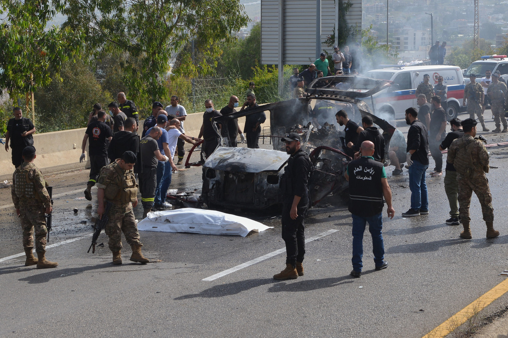 Security forces and emergency responders gather around a charred vehicle at the scene of an Israeli airstrike that hit a car, as a covered body lies on the ground, in the coastal town of Jiyeh, south of Beirut, Lebanon, Wednesday, May 13, 2026. (AP Photo/Mustafa Jamalddine)