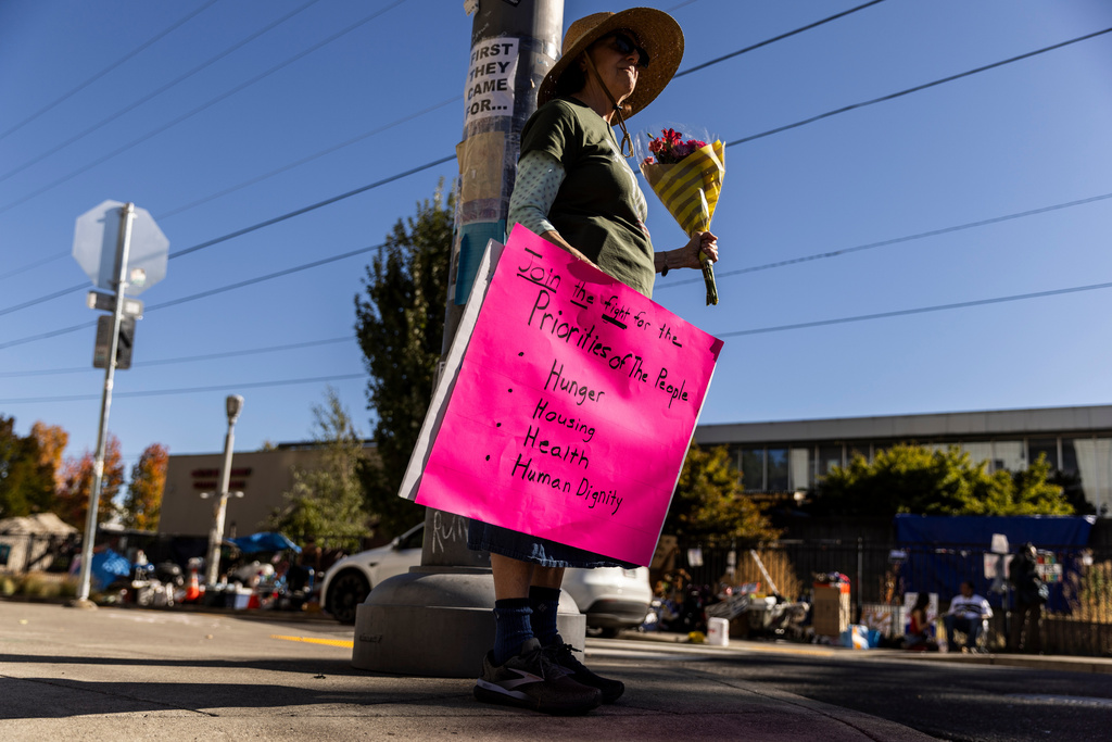 Katherine Foldes, 76, whose grandparents died at the Nazi concentration camps during World War II, holds a sign and flowers in protest outside a United States Immigration and Customs Enforcement (ICE) facility in Portland, Ore., Monday, Oct. 6, 2025. (Stephen Lam/San Francisco Chronicle via AP)