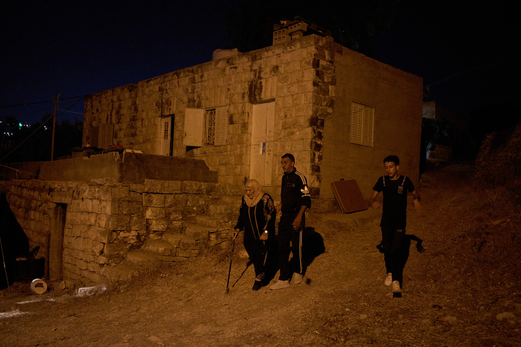 Khadra Dar Khalil, left, walks toward an area where members of her family and neighbours sit outside their homes to help prevent Israeli settler attacks in the West Bank town of Sinjil, Monday, July 27, 2026. (AP Photo/Leo Correa)