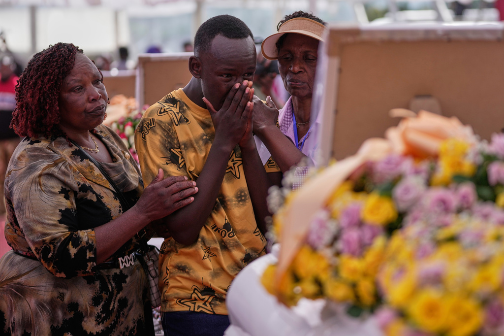 A relative grieves while standing between caskets carrying the remains of girls who died in the Utumishi Academy school fire during a memorial service at Gilgil Stadium, Nakuru County, Kenya, Friday, June 12, 2026. (AP Photo/Brian Inganga)
