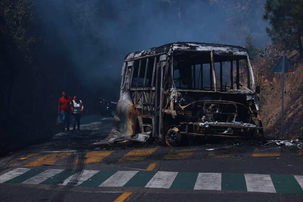 Pedestrians walk past a charred vehicle after it was set on fire, on a road in Cointzio, Michoacán state, Mexico, Sunday, Feb. 22, 2026, after the death of the leader of the Jalisco New Generation Cartel, Nemesio Rubén Oseguera Cervantes, known as "El Mencho." (AP Photo/Armando Solis)