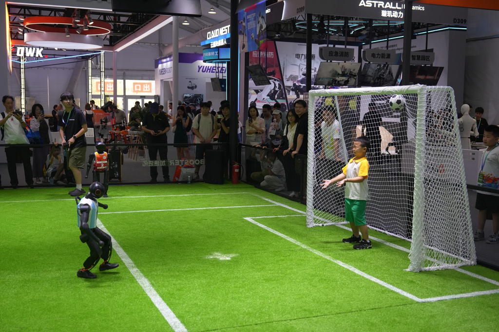 A child reacts on a goal post as he plays soccer with a robot at a booth during the World Robot Conference at the Beiren Yichuang International Convention and Exhibition Centre in Beijing, Wednesday, Aug. 19, 2026. (AP Photo/Andy Wong)
