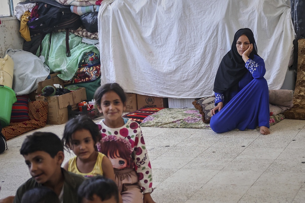A woman and her kids sit at a school sheltering displaced Syrian Bedouins from the Sweida region, forced from their homes after clashes between Druze militias and Bedouin groups, in the village of Abtaa in rural Daraa, Syria, Aug. 15, 2025. (AP Photo/Ghaith Alsayed)