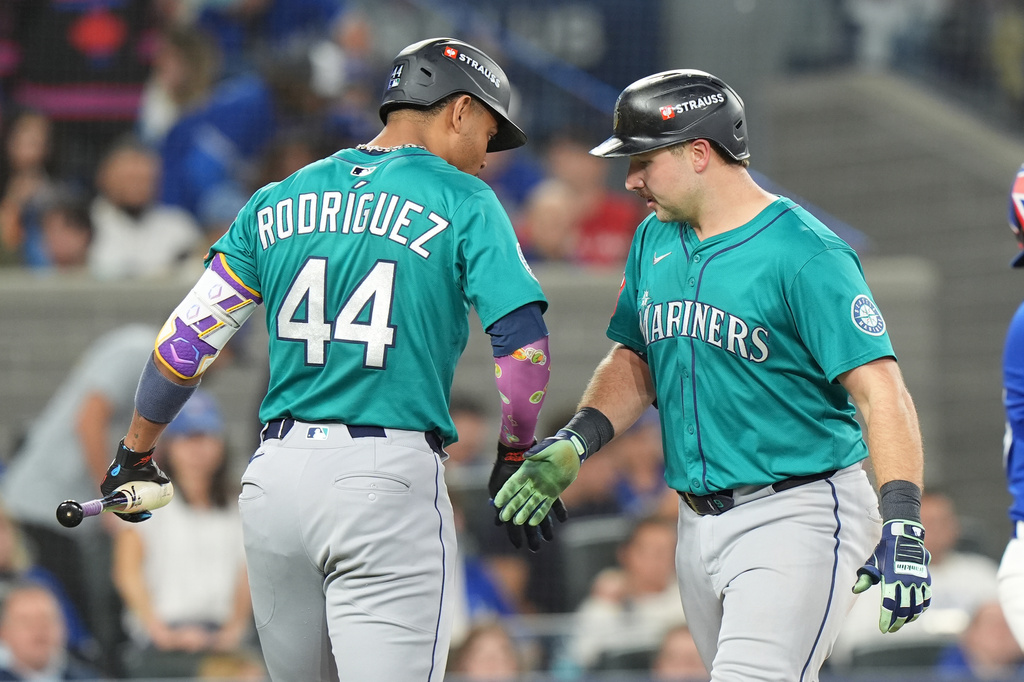 Seattle Mariners' Julio Rodríguez (44) congratulates teammate Cal Raleigh, right, as Raleigh crosses home plate after hitting a solo home run off Toronto Blue Jays pitcher Kevin Gausman during the sixth inning in Game 1 of baseball's American League Championship Series in Toronto, Sunday, Oct. 12, 2025. (Frank Gunn/The Canadian Press via AP)