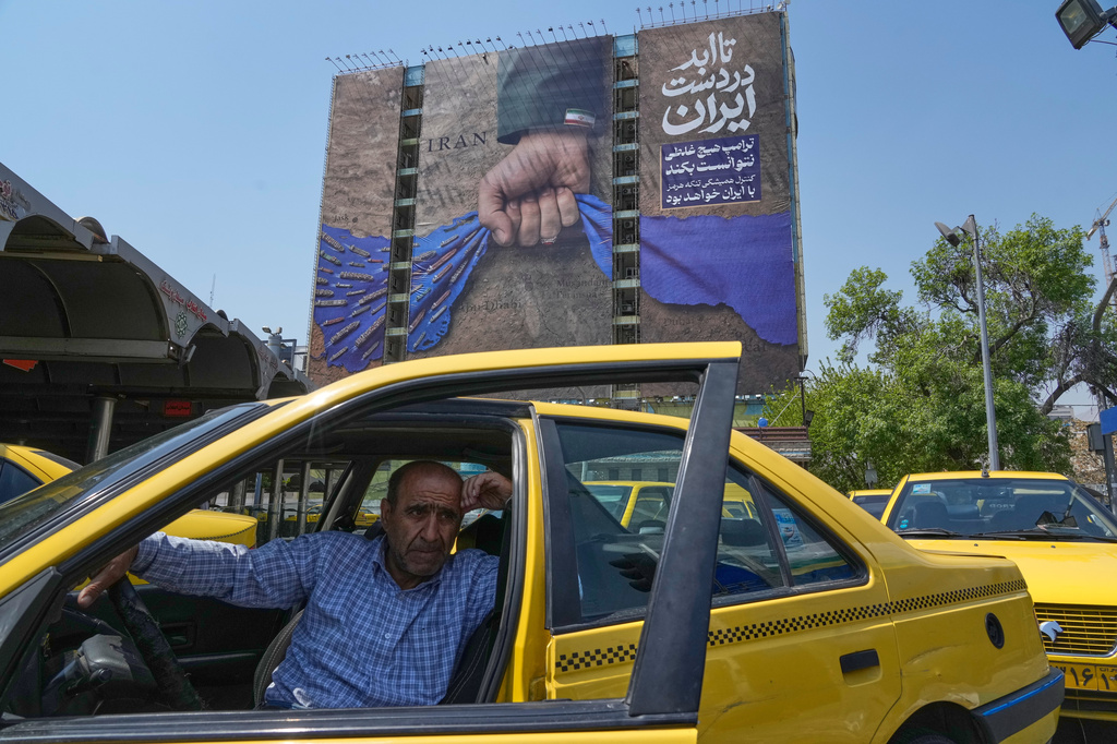 A taxi driver waits for passengers in front of a billboard that shows a graphic depicting a military personnel's hand holding the Strait of Hormuz in his fist with signs which read in Farsi: "In Iran's hands forever," "Trump couldn't do a damn thing," "The control of Strait of Hormuz will be Iran's forever," in Vanak Square in northern Tehran, Iran, Thursday, April 16, 2026. (AP Photo/Vahid Salemi)