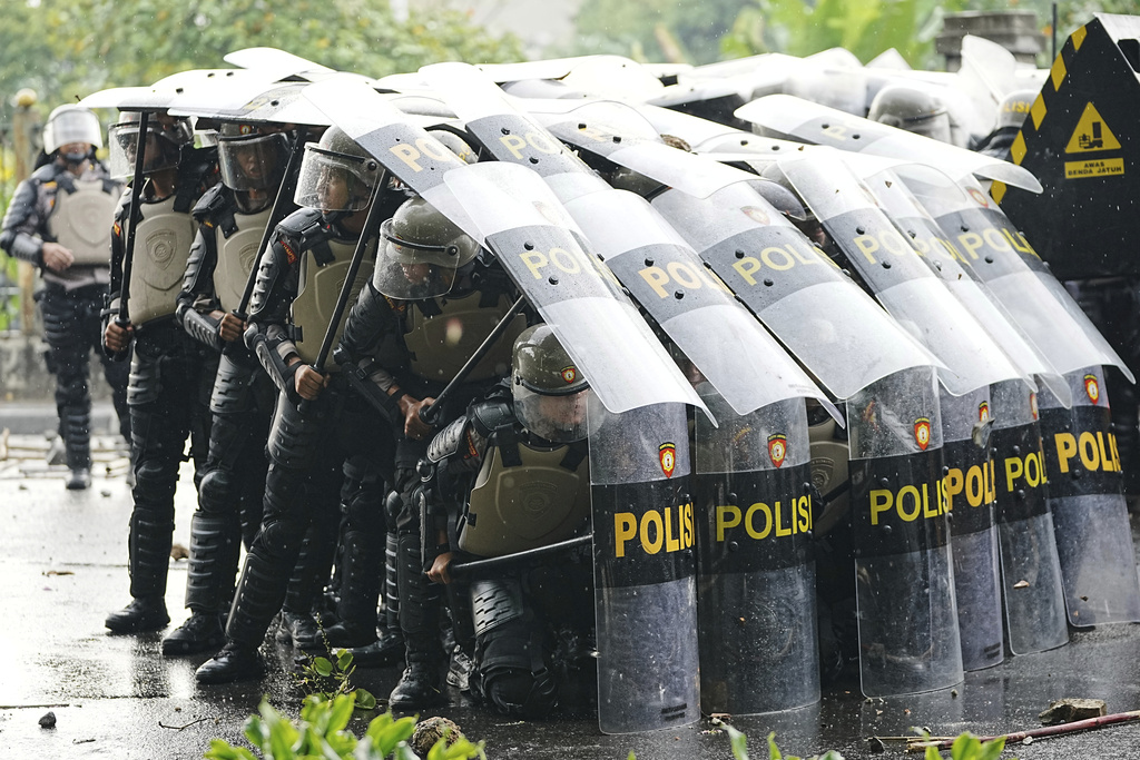 Riot police officers take defensive position as they clash with protesters during a protest against lavish allowances given to parliament members, in Jakarta, Indonesia, Thursday, Aug. 28, 2025. (AP Photo/Achmad Ibrahim)