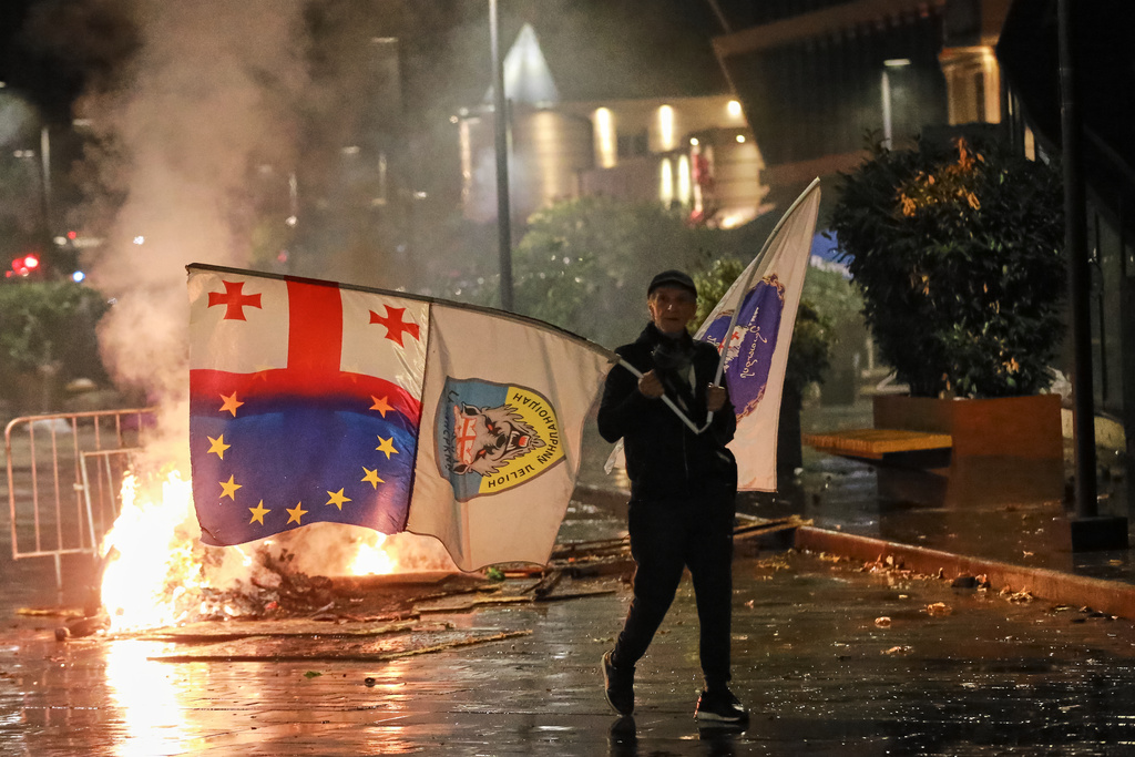 A demonstrator with a Georgian national, EU and other flags walks in front of police line during an opposition rally in the city center of Tbilisi, Georgia, on Saturday, Oct. 4, 2025, boycotting the municipal elections and calling for the release of political opponents. (AP Photo/Zurab Tsertsvadze)