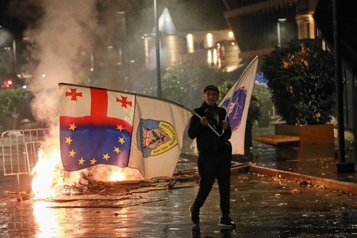 A demonstrator with a Georgian national, EU and other flags walks in front of police line during an opposition rally in the city center of Tbilisi, Georgia, on Saturday, Oct. 4, 2025, boycotting the municipal elections and calling for the release of political opponents. (AP Photo/Zurab Tsertsvadze) A demonstrator with a Georgian national, EU and other flags walks in front of police line during an opposition rally in the city center of Tbilisi, Georgia, on Saturday, Oct. 4, 2025, boycotting the municipal elections and calling for the release of political opponents. (AP Photo/Zurab Tsertsvadze)