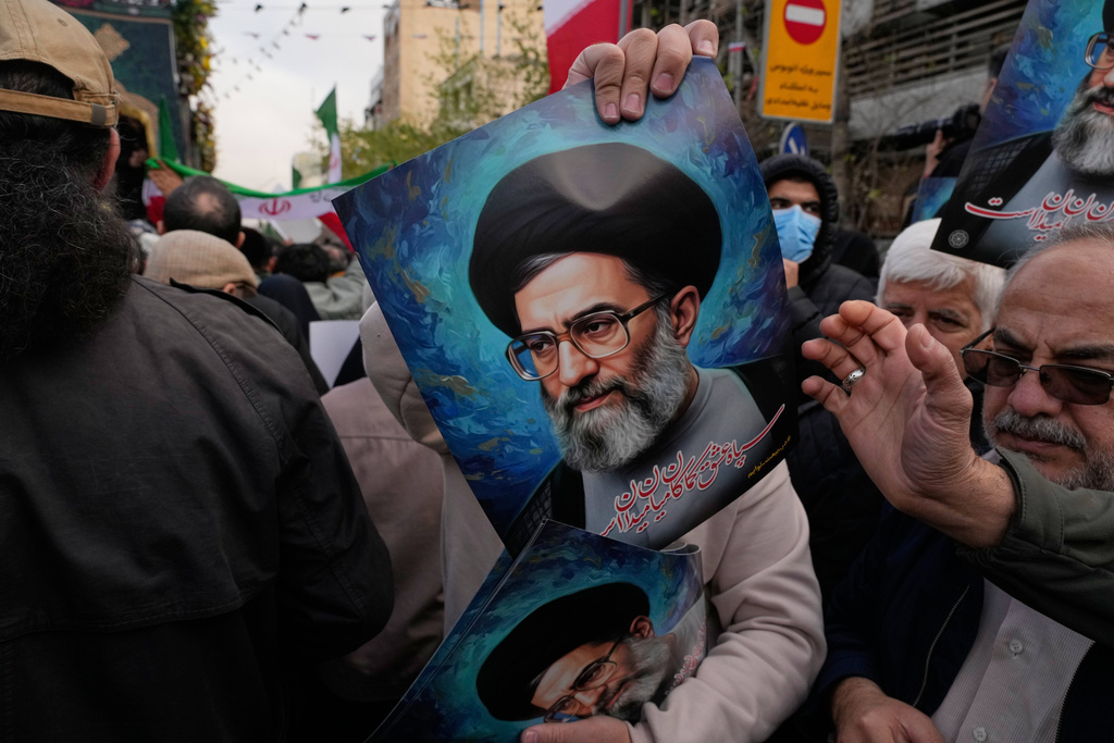 A man hands out posters of the Iranian Supreme Leader Ayatollah Ali Khamenei during a funeral ceremony for a group of security forces, who were killed during anti-government protests, in Tehran, Iran, Wednesday, Jan. 14, 2026. (AP Photo/Vahid Salemi)