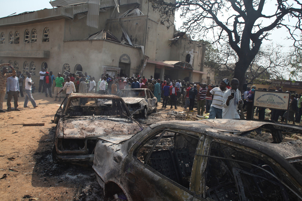 FILE- Onlookers gather around burnt out cars at the site of a bomb blast at St. Theresa Catholic Church in Madalla, Nigeria, Sunday, Dec. 25, 2011. (AP Photo/Sunday Aghaeze, File)